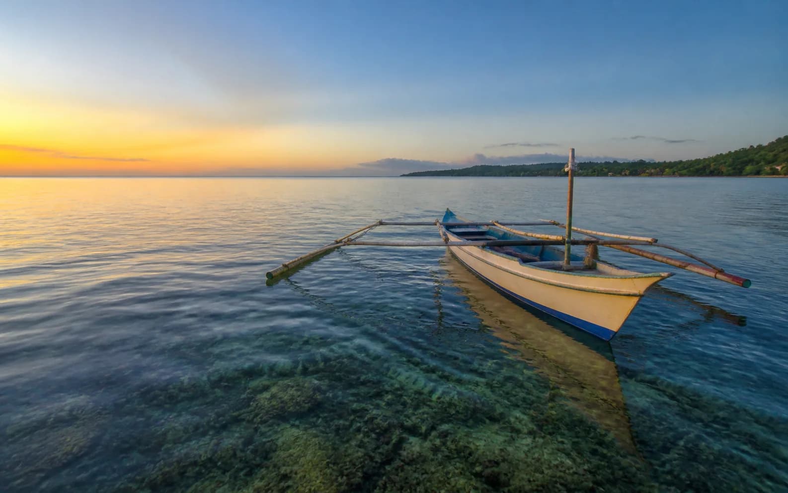 A traditional bangka outrigger floating above the reef at dawn